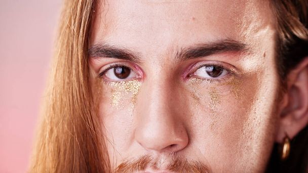 Make-up, oči a portrét gen z muž s vážným výrazem na tváři s růžovým pozadím. Zlato, třpytivé slzy a umění, zvětšení oční kosmetiky na nebinárním, transgender nebo genderově neutrálním lgbt modelu. - Fotografie, Obrázek