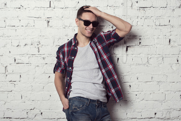Молодой привлекательный мужчина хипстер в солнечных очках, рука в волосах улыбается
 - Фото, изображение