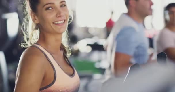 Fitness, happy and sporty woman doing a cardio workout while rinning on a treadmill and smiling at the camera. Athletic, fit and real people being active and training together at a health club. - Video