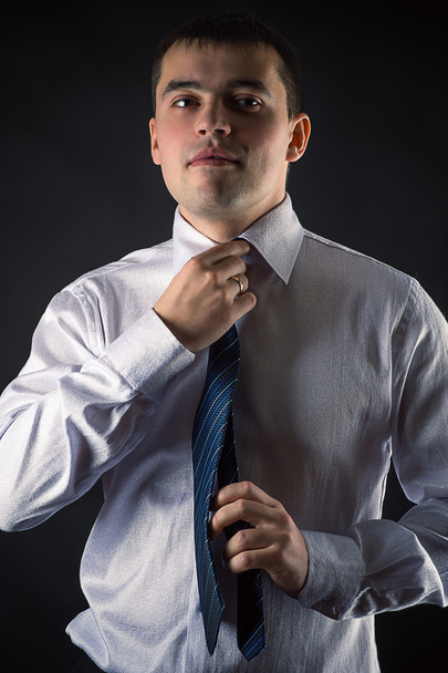 Handsome businessman corrects tie isolated on black background - Photo, Image