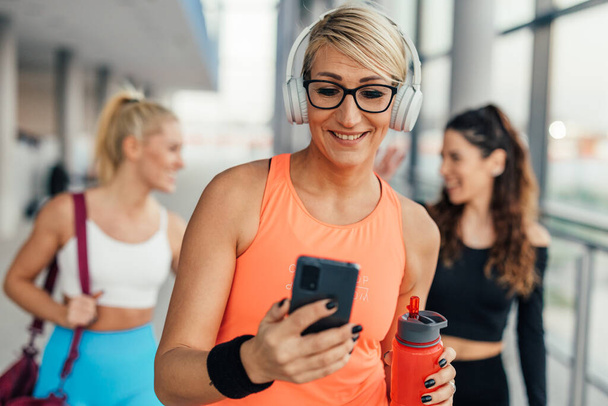 Happy middle adult woman looks at her phone in the gym - Fotoğraf, Görsel