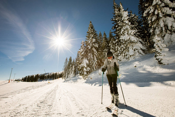 Une seule jeune femme profite d'une journée ensoleillée de ski d'hiver, vêtue d'un équipement complet de neige avec des bottes de ski et des lunettes de soleil - Photo, image