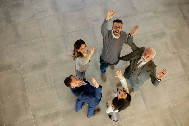 Αεροφωτογραφία σε χαρούμενες επιχειρήσεις οι άνθρωποι σηκώνουν τα χέρια μαζί με χαρά και επιτυχία στο διάδρομο του γραφείου. Επιτυχής και ομαδική εργασία - Φωτογραφία, εικόνα