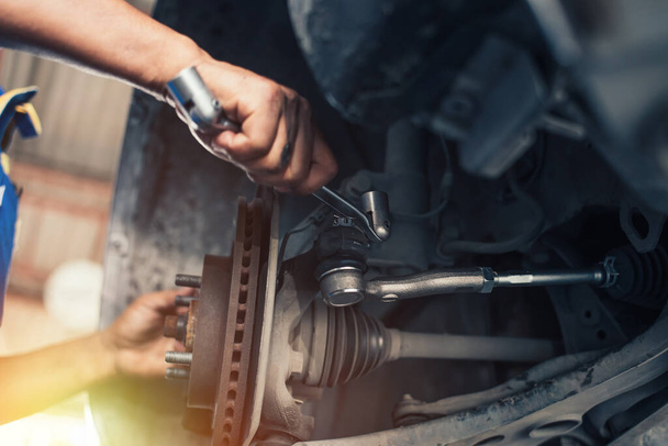 In een reparatiewerkplaats trekt een automonteur de vering van een verhoogd voertuig met een moersleutel aan.. - Foto, afbeelding