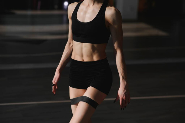 Chica atlética haciendo ejercicio para el glúteo con banda de resistencia sobre fondo gris. Mujer de fitness haciendo ejercicio. - Foto, imagen