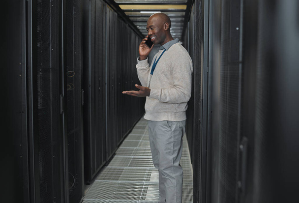 Server room, phone call and man for system update, technician power or cyber security backup communication. Person, african engineering or programmer in information technology talking on smartphone. - 写真・画像