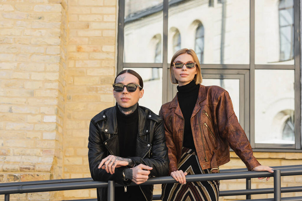 stylish couple in trendy sunglasses and leather jackets standing outdoors  - Photo, image