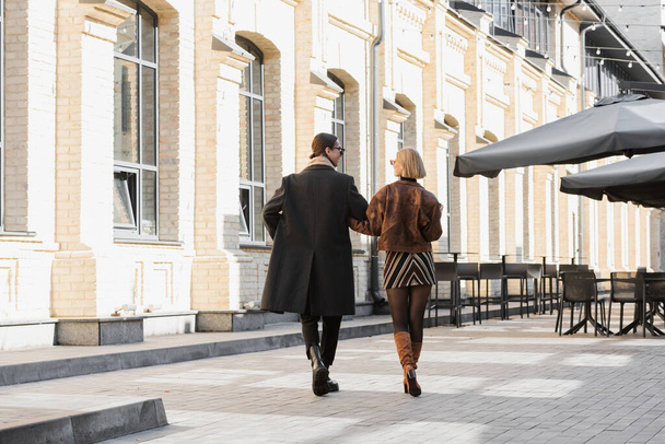 full length of blonde woman in trendy leather jacket walking with boyfriend on street   - Zdjęcie, obraz
