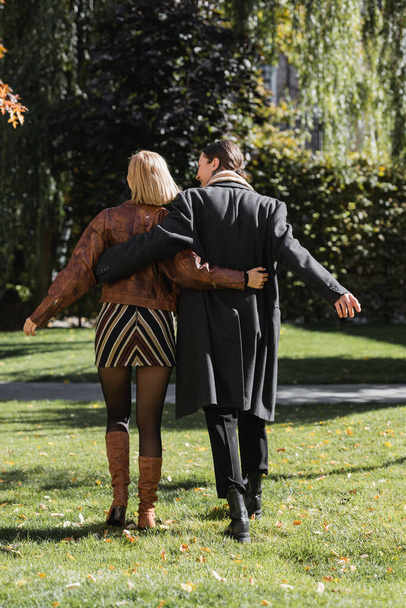 назад вид молодой пары обнимающей во время прогулки в парке во время свидания  - Фото, изображение