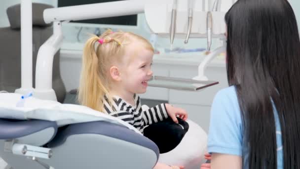 radość w fotelu u dentysty dziewczyna spotyka lekarza uśmiecha się nieśmiały spojrzenia w oczy lekarz prostuje bluzkę włosy i mówi o narzędziach strach doświadcza przyjaźni najnowsza technologia stomatologiczne biuro - Materiał filmowy, wideo