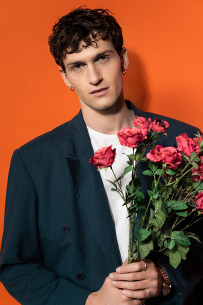 Portrait of man in jacket and t-shirt holding roses on orange background  - Foto, immagini