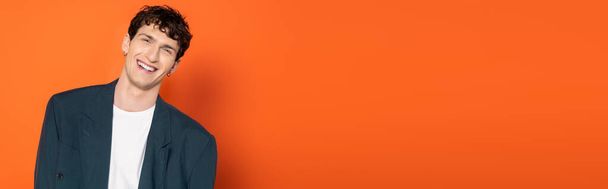 Smiling man in blue jacket and t-shirt looking at camera on orange background, banner  - Photo, Image