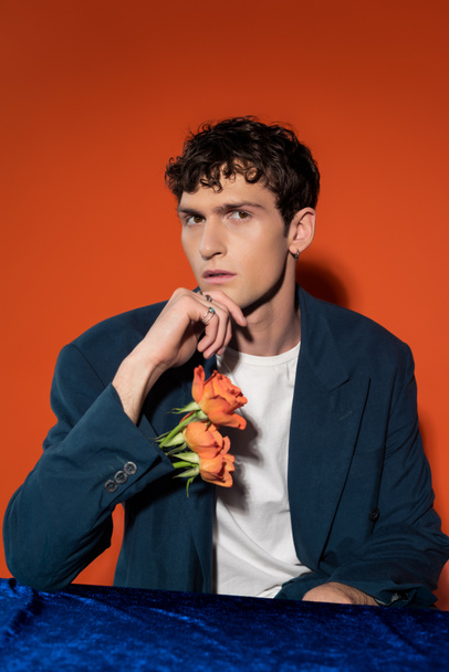 Stylish young man with flowers in sleeve of jacket looking at camera on red background - Foto, Imagen