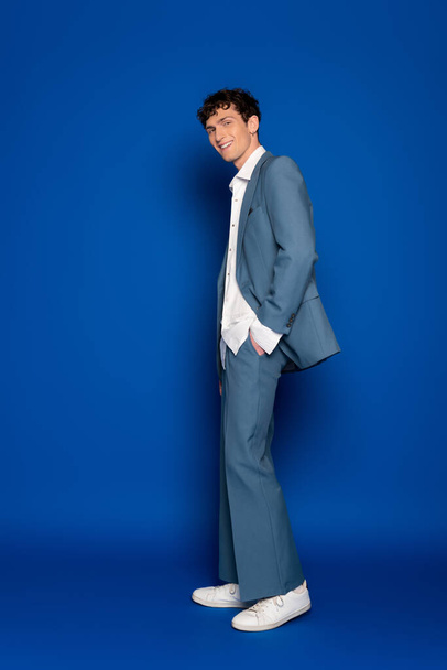 Повна довжина модного чоловіка в костюмі і сорочці позує на синьому фоні
  - Фото, зображення