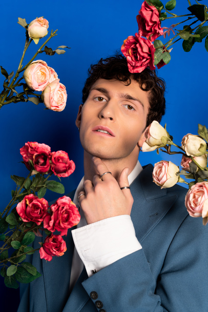 Divatos fiatal férfi dzsekiben pózol közel rózsák kék háttér  - Fotó, kép