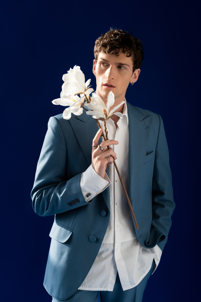 Fashionable model in suit holding magnolia flowers isolated on navy blue with sunlight  - Photo, Image