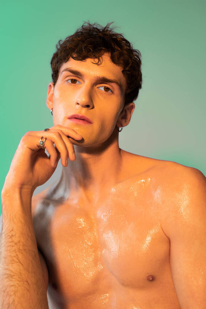 Portrait of young shirtless man with oil on skin looking at camera on green background  - Φωτογραφία, εικόνα