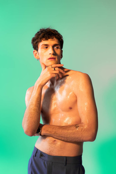 Shirtless man with oil on body posing and looking away on green background - Foto, afbeelding