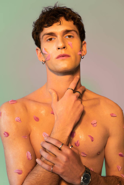 Shirtless man with petals on body touching neck on colorful background  - Valokuva, kuva