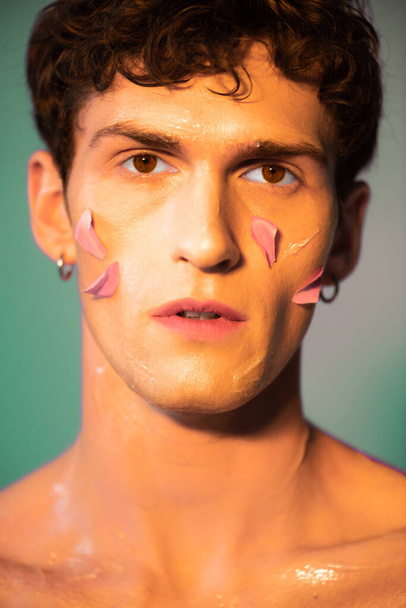 Portrait of man with petals on face looking at camera on colorful background  - Photo, Image
