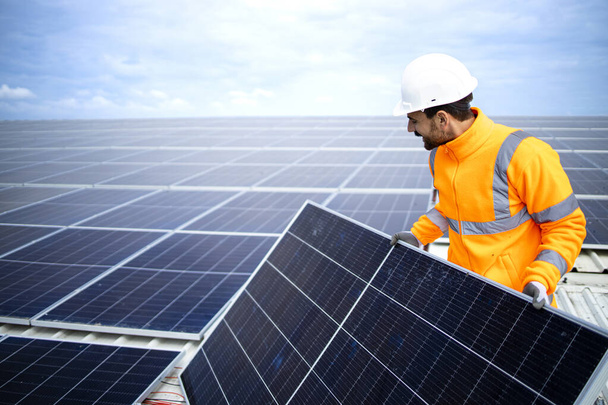 Βιομηχανικός εργαζόμενος που εγκαθιστά ηλιακούς συλλέκτες στην οροφή του εργοστασίου για φθηνή βιώσιμη ενέργεια ή ηλεκτρική ενέργεια. - Φωτογραφία, εικόνα
