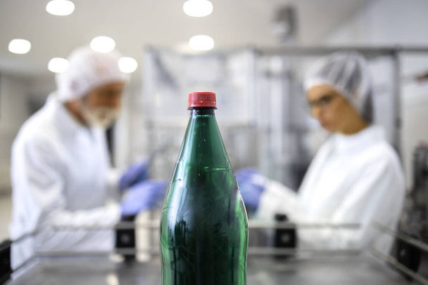 Water bottling plant and production line workers in background working in food and drink industry. - Foto, imagen