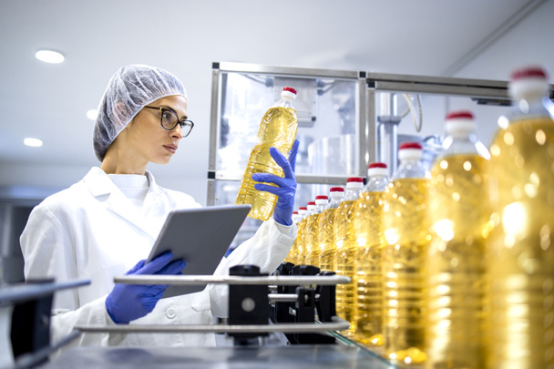 Инспектор по пищевым продуктам или технолог, осуществляющий контроль качества растительного масла в бутылках внутри завода. - Фото, изображение