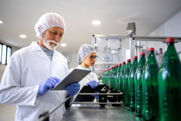 Skoncentrowani pracownicy kontroli jakości kontrolujący produkcję butelkowanej wody pitnej w fabryce napojów. - Zdjęcie, obraz