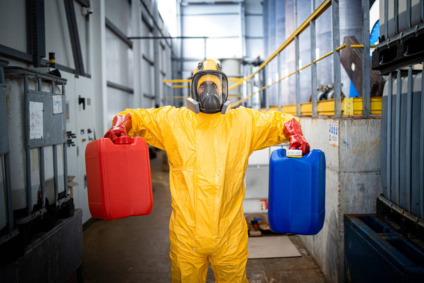Химический работник в защитном костюме и противогазе, перевозящий канистры на завод. - Фото, изображение