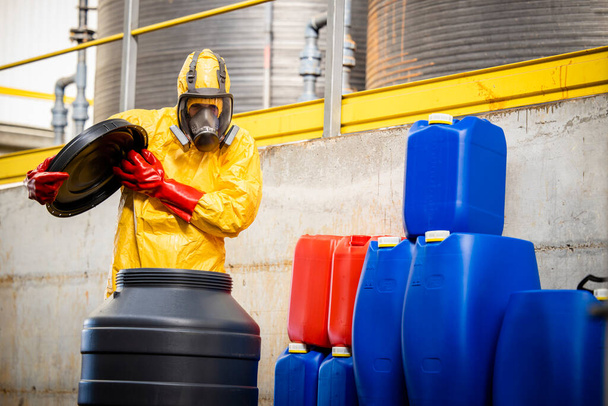 Chemical technologist in hazmat suit and gas mask opening barrel with aggressive substances and fumes in chemicals production plant. - Photo, Image