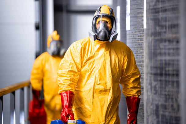 Portret van een industrieel werknemer in een beschermingspak voor hazmatten en gasmaskers die in een chemische fabriek werken. Op de achtergrond grote tanks met zuur en fabriek interieur. - Foto, afbeelding