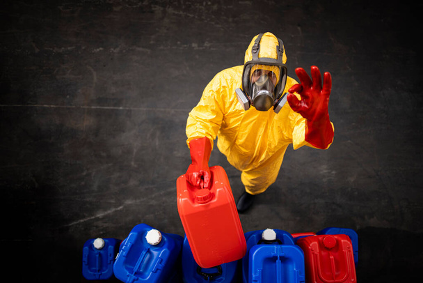 Professionele werknemer in hazmat beschermingspak en gasmasker werken met gevaarlijke chemische stoffen in de fabriek. - Foto, afbeelding