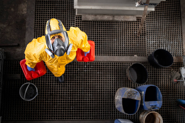 Vista superior del trabajador de fábrica con traje de materiales peligrosos y máscara de gas mirando hacia la cámara. - Foto, imagen