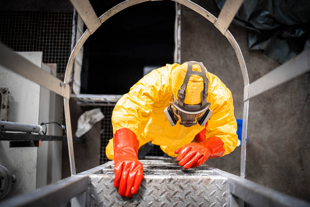 Top view of worker in protective suit and gas mask climbing metal industrial ladder inside chemicals factory. - Foto, afbeelding