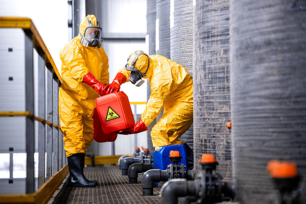 Factory workers carefully handling toxic and dangerous biohazardous waste in chemicals factory. - Foto, Imagen