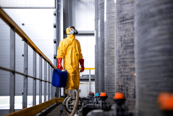 Заводской работник в защитном оборудовании проверяет количество химических веществ внутри большого резервуара. - Фото, изображение