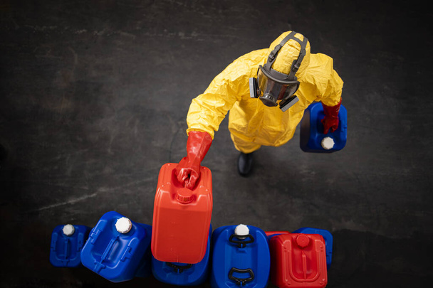 Professionele werknemer in hazmat beschermingspak en gasmasker werken met gevaarlijke chemische stoffen in de fabriek. - Foto, afbeelding