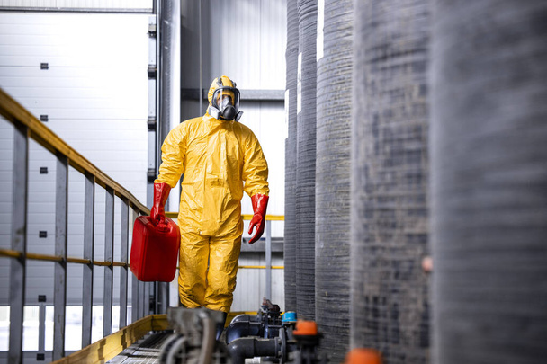 Factory worker in protective equipment and gas mask carrying dangerous chemicals. - Foto, Imagen