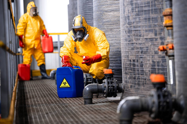 Trained factory workers carefully handling toxic and dangerous biohazardous waste in chemicals factory. - Zdjęcie, obraz