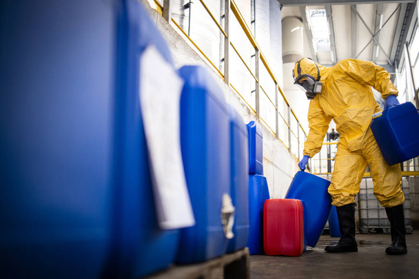 Worker wearing protection suit and gas mask working in chemicals production factory. Carrying acid plastic containers for zinc galvanizing industry. - Foto, Imagen