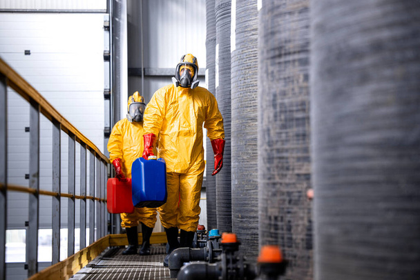 Sarı takım elbiseli, gaz maskeli ve eldivenli tam korumalı işçiler tehlikeli kimyasallar ve maddelerle uğraşıyorlar.. - Fotoğraf, Görsel