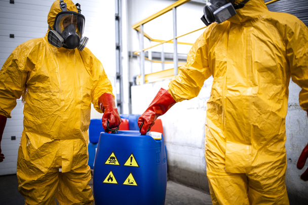 Chemicals production factory. Experienced workers fully protected in gas mask carrying hazardous and toxic waste in chemical plant. - Zdjęcie, obraz