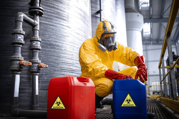 Chemicals industry production. Fully protected worker in yellow suit, gas mask, gloves and boots working with hazardous waste. - Foto, Imagen