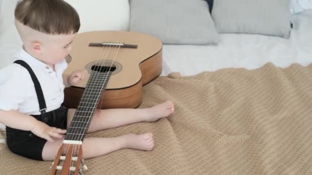 Un bambino di 2 anni suona la chitarra. Il bambino sta giocando da solo. 4k video - Filmati, video