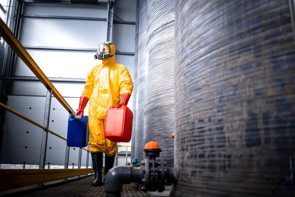 Chemicals production industry interior and worker in protection suit and gas mask walking by acid tanks. - Foto, Imagen