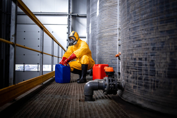 Industrial chemicals production. Experienced worker in protection suit, gas mask, gloves and boots opening canister with acid in zinc galvanizing factory. - Foto, Imagen