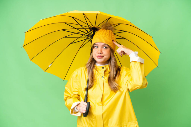 Yağmura dayanıklı ceketi ve şemsiyesi olan genç bir kız izole edilmiş krom anahtar geçmişi üzerinde şüpheleri ve düşünceleri var. - Fotoğraf, Görsel