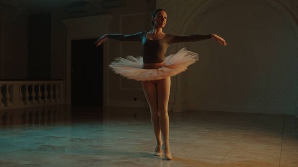 Cinematic shot of graceful female ballet dancer on choreography rehearsal in theater lobby, practicing elegant movements. Ballerina in tutu before performance in opera. Classical theatrical ballet art - Photo, image