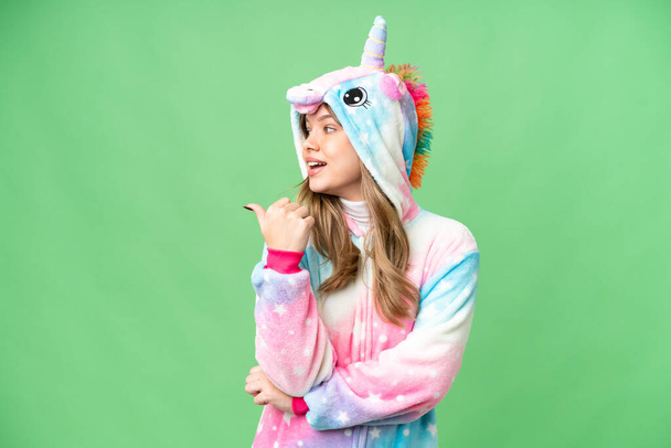 Young girl with unicorn pajamas over isolated chroma key background pointing to the side to present a product - Photo, Image