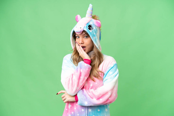 Chica joven con pijama de unicornio sobre fondo de croma clave aislada sorprendida y sorprendida mientras mira a la derecha - Foto, Imagen